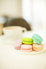 Cup of coffee and testy macaroons on white table in cafe.