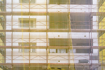 Building facade renovation, old house reconstruction, repair. Scaffold in front of building facade covered with yellow transparent fabric