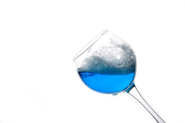 Glass with splashing blue drink, isolated on a white background. Splash of a trendy blue wine. Cocktail with blue liquid in glass with copy space for text. 