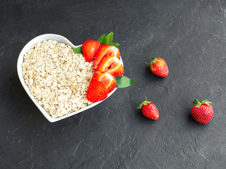 Oatmeal with milk. Porridge with milk. Diet Breakfast. Ripe strawberries, oatmeal. Heart shape ceramic plate on black backround