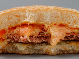 bitten big burger with cutlet cheese and tomato on a gray background
