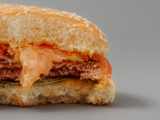 bitten big burger with cutlet cheese and tomato on a gray background