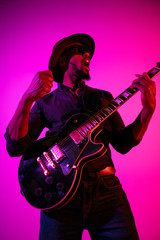 Obraz na płótnie Canvas Young african-american musician playing the guitar like a rockstar on gradient purple-pink background in neon light. Concept of music, hobby. Joyful attractive guy improvising and singing a song.