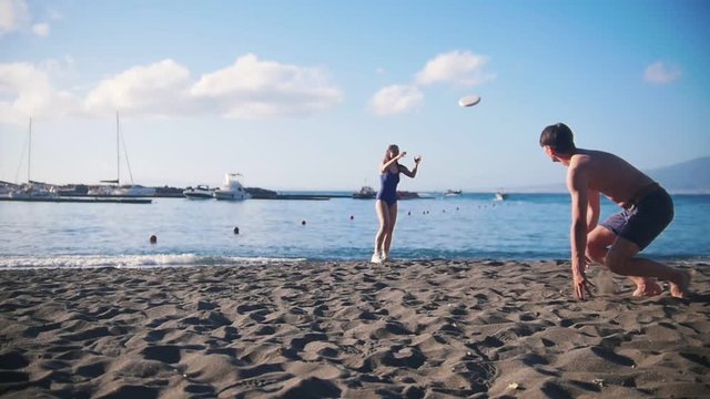 A young man playing frisbee on the beach with his girlfriend. Throwing the disc to her