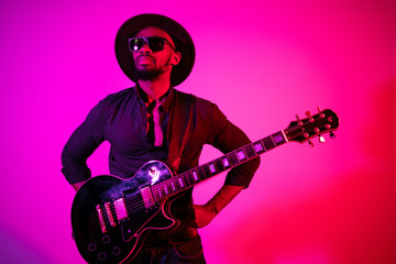 Young african-american musician playing the guitar like a rockstar on gradient purple-pink...