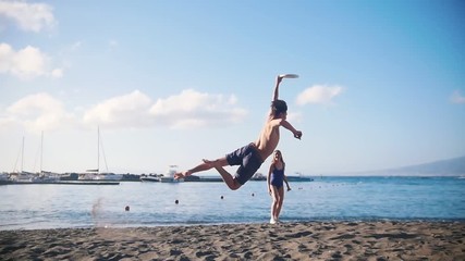 A young man playing frisbee on the beach with his female friend. Catching the disc and falling on the sand - Powered by Adobe