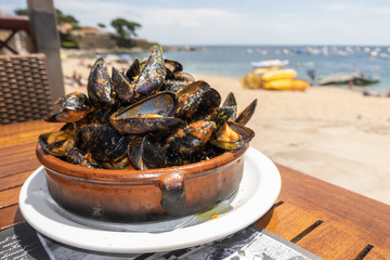 mussels cooked with sauce served in a clay pot on a table at the beach