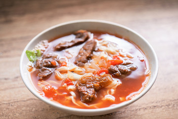 Beef noodle ramen meal with tomato sauce broth in bowl on bright wooden table, famous chinese style food in Taiwan, close up, top view, copy space