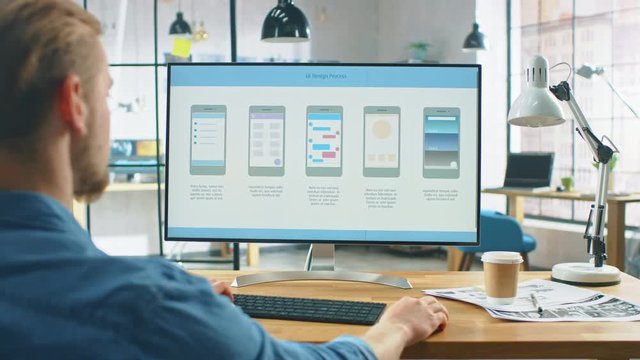 Young Professional Works on a Laptop at His Desk in the Creative Office. Notebook Screen Shows Mobile Phone Application Design, Software UI Development. In the Background Creative Modern Office