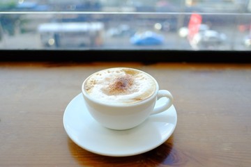 A cup of hot cappuccino coffee on wooden counter with blurred a city view