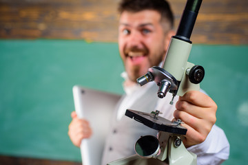 Happy bearded man in science class. E-learning. Biology or chemistry concept. Scientist or docent with laptop and microscope. Male teacher with computer and microscope. Selective focus on microscope.