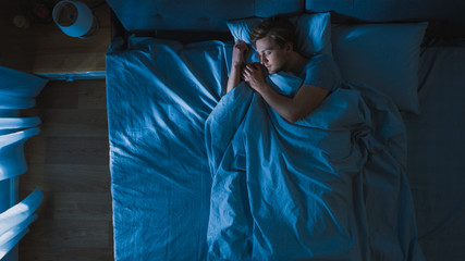 Top View of Handsome Young Man Sleeping Cozily on a Bed in His Bedroom at Night. Blue Nightly...