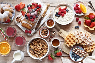 Happy breakfast with granola, oatmeal porridge, smoothies, fresh waffles, sweets, fruits and berries.