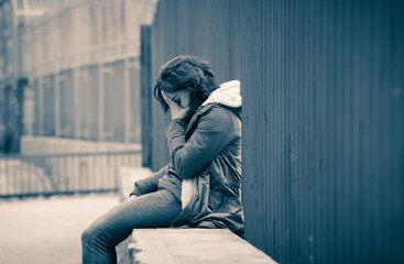 Depressed young woman sitting on urban city street overwhelmed a