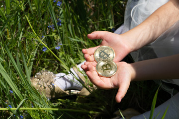 Bitcoins in children's hands. Children's hands hold gold bitcoins on the background of green grass.