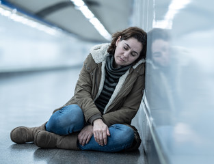 Young desperate adult woman sitting on the ground on subway unde