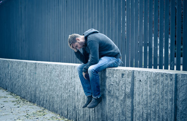 Unhappy depressed caucasian male sitting on urban street feeling