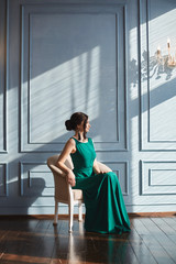 Fashionable and beautiful brunette model girl with stylish hairstyle in green evening dress sits in...