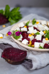 Salad of beet, feta cheese, onion and olive oil in a white plate, on a hand-knitted napkin all on a gray background.