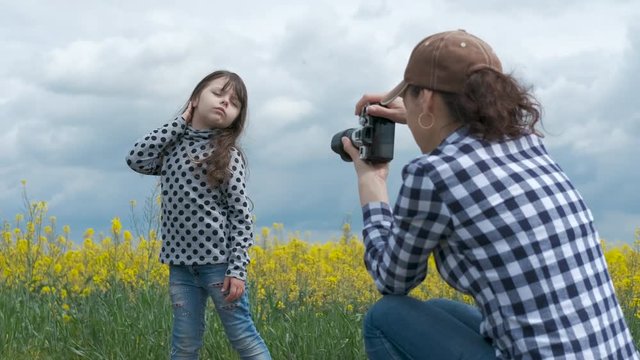 Mother takes a picture of a child. A woman photographs a charming little girl on a camera in nature.