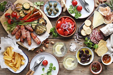 Grill party table concept with grilled sausage, potato fries,vegetable,sappetizers and tomato salad. Summer outdoor dinner table .