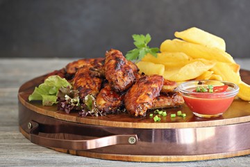Oven baked spicy barbecue chicken wings with potato fries.
