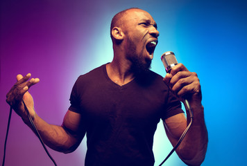 Young african-american jazz musician singing a song on gradient purple-blue background. Concept of...