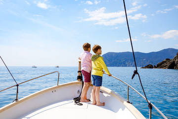 Two adorable school kid boys, best friends enjoying sailing boat trip. Family vacations on sea on sunny day. Children smiling. Brothers, schoolchilden, siblings, best friends having fun on yacht. - obrazy, fototapety, plakaty