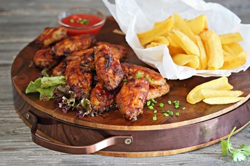 Oven baked spicy barbecue chicken wings with potato fries.