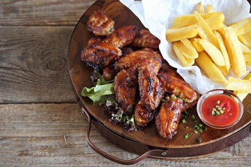 Oven baked spicy barbecue chicken wings with potato fries.