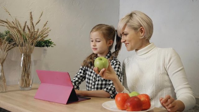 Attractive daughter is taking good looking apple from smiling woman at kitchen.