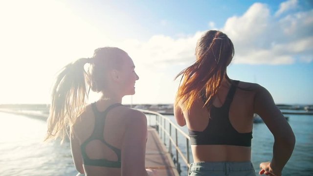 Two young women jogging on the bridge towards the sea port in sunny day