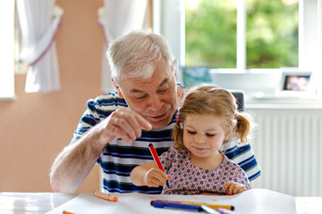 Cute little baby toddler girl and handsome senior grandfather painting with colorful pencils at...