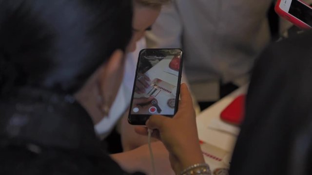 Woman with brown hair filming with her smartphone a practitioner of eyelash extensions during a conference on eyelash extensions in Prague. Black and red smartphones. Recording video.