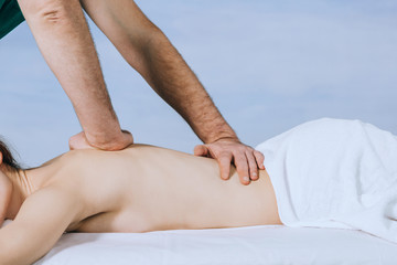 man's hands of masseur is doing massage shoulder of a young woman  27 years oldon a blue background.