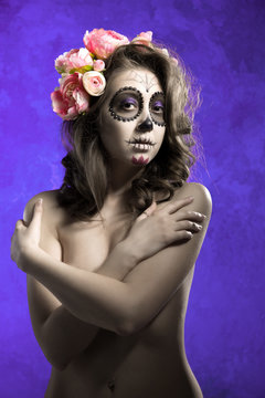 Young half-naked girl in a wreath of flowers on a purple background. Girl skeleton. Sugar skull of dead bride deadly pale skin. 