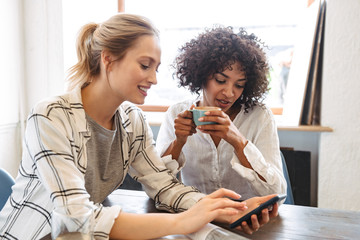 Two happy young women friends sitting at the cafe