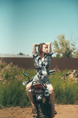 Plakat Young beautiful girl posing sitting on a motorcycle outdoors