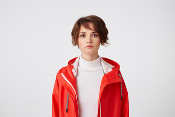 Portrait of young cute short haired girl dressed in white golf and red rain coat, looking at the...