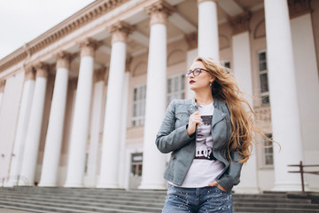 Young caucasian blondie hipster woman with long curly hairstyle in eye glasses in the city street. Freelance, freedom, beauty, happy lifestyle concept