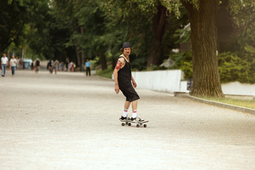 Skateboarder doing a trick at the city's street in cloudly day. Young man in sneakers and cap riding and longboarding on the asphalt. Concept of leisure activity, sport, extreme, hobby and motion.