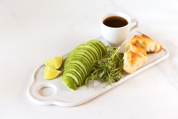 Breakfast with avocado, bun, pea sprouts, lime, pesto and coffee.