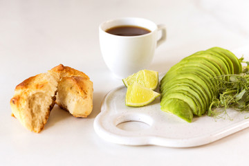 Breakfast with avocado, bun, pea sprouts, lime, pesto and coffee.