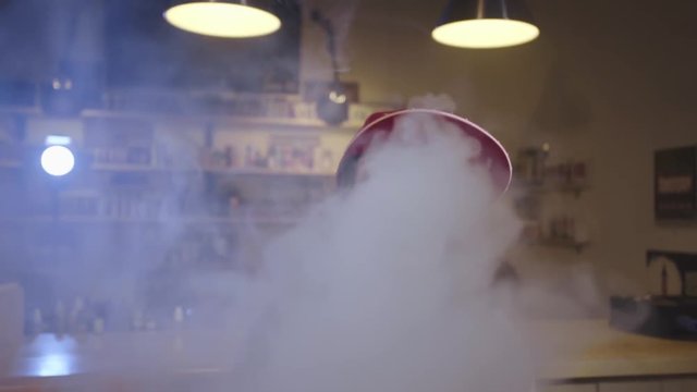Young pretty woman in red cap smoke an electronic cigarette at the vape shop. Closeup. Slow motion.