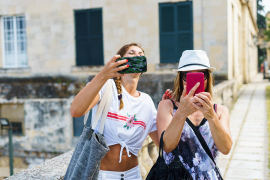 Two beautiful tourist women taking selfie pictures using mobile phone in the old town street in a summer day