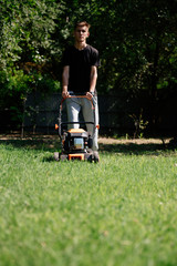 Gardener mows the lawn in the garden with a lawn mower in summer