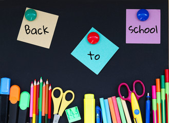 Colorful various school stationary with Back to school text on note papers pinched to blackboard background. Copy space. Back to school concept