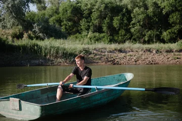 Foto op Canvas Young man floats on a wooden boat with oars © bo.kvk