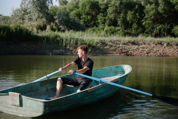 Fototapeta na wymiar Young man floats on a wooden boat with oars