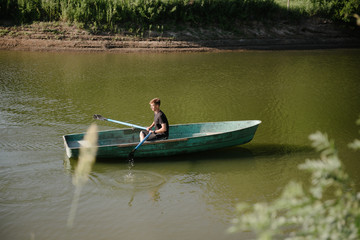 Young man floats on a wooden boat with oars